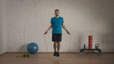 Atletik fitness koçu online dersler için ev stüdyosunda egzersiz yapıyor. Spor giyimli bir adam ip atlama egzersizi yapıyor..