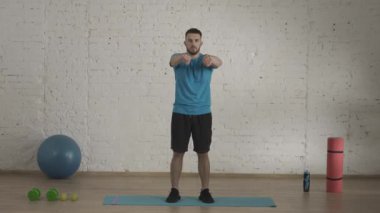 Evde kişisel spor eğitimleri. Atletik erkek fitness koçu çevrimiçi dersler için ev stüdyosunda egzersiz yapıyor. Spor kıyafetli bir adam dirseklerini çeviriyor ve kolları ısınıyor. Sağlık sigortası konsepti. HDR