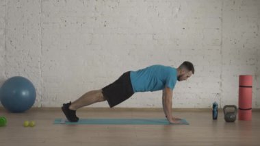 Evde kişisel spor eğitimleri. Atletik erkek fitness koçu çevrimiçi dersler için ev stüdyosunda egzersiz yapıyor. Spor kıyafetli bir adam kalas egzersizinde aktif olarak koşuyor. Sağlık konsepti HDR
