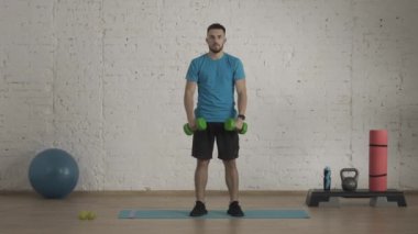 Evde kişisel spor eğitimleri. Atletik erkek fitness koçu çevrimiçi dersler için ev stüdyosunda egzersiz yapıyor. Spor kıyafetli bir adam halterle kol kaldırma egzersizi yapıyor. Sağlık hizmetleri kavramı