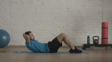 Yakın plan çekim. Atletik erkek fitness koçu çevrimiçi dersler için ev stüdyosunda egzersiz yapıyor. Spor kıyafetli bir adam klasik karın kasları egzersizi yapıyor. Sağlık sigortası konsepti. HDR BT2020 HLG Malzemesi.