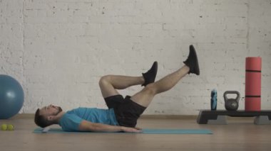 Atletik erkek fitness koçu çevrimiçi dersler için ev stüdyosunda egzersiz yapıyor. Spor kıyafetli bir adam karın kası egzersizi için bacak döngüsü yapıyor. Sağlık sigortası konsepti. HDR BT2020 HLG Malzemesi.