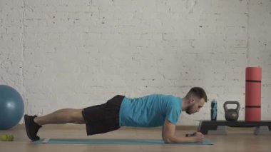 Yakın plan çekim. Evde kişisel spor eğitimleri. Atletik erkek fitness koçu çevrimiçi dersler için ev stüdyosunda egzersiz yapıyor. Spor kıyafetli bir adam statik dirsek tahtası egzersizi yapıyor. HDR BT2020 HLG