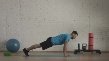 Evde kişisel spor eğitimleri. Atletik erkek fitness koçu çevrimiçi dersler için ev stüdyosunda egzersiz yapıyor. Spor kıyafetli bir adam düz kollar üzerinde statik tahta yapıyor. HDR BT2020 HLG
