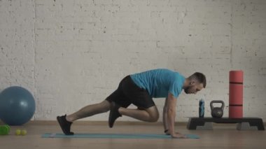 Yakın plan çekim. Evde kişisel spor eğitimleri. Atletik erkek fitness koçu çevrimiçi dersler için ev stüdyosunda egzersiz yapıyor. Spor kıyafetli bir adam kalas egzersizinde aktif olarak koşuyor. HDR BT2020