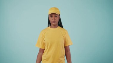 Kurye hizmeti konsepti. Sarı şapkalı ve tişörtlü bir kadının portresi elinde kahve tutacağı ve içinde yiyecek olan bir kese kağıdı tutuyordu. Paket servis ürünleri. Mavi arkaplanda izole.