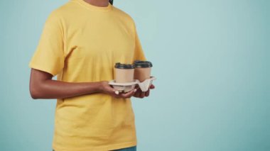 Yakın plan çekim. Kurye hizmeti konsepti. Sarı tişörtlü bir teslimatçının portresi kadın müşteriye kahve fincanı veriyor. Mavi arkaplanda izole.