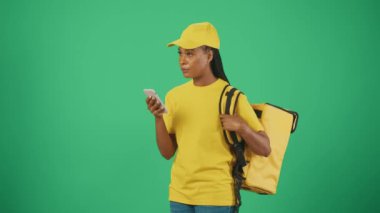 Kurye hizmeti konsepti. Sarı şapkalı ve tişörtlü teslimatçı kadının portresi müşterisiyle buluşup emir vermeyi bekliyor. Yeşil arkaplanda izole.
