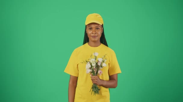 宅配サービスのコンセプト 黄色い帽子とTシャツの配達女性の肖像画は 空の領域を指して花束を保持し 親指を示しています 緑の背景に孤立した — ストック動画