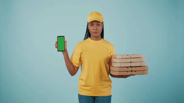 一个头戴黄帽 头戴T恤 拿着披萨盒和智能手机的送货妇女的画像 被蓝色背景隔离了广告区 工作空间模型 — 图库照片
