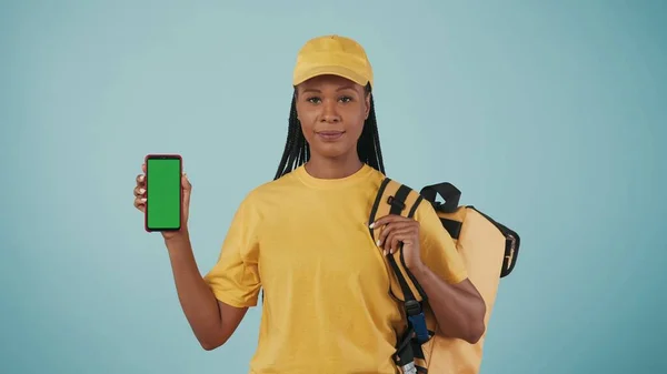 一个带着背包 冰箱和智能手机 头戴黄色帽子的送货妇女的画像 被蓝色背景隔离了广告区 工作空间模型 — 图库照片