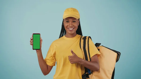 一个头戴黄色帽子 背负式冰箱和智能手机的送货妇女的画像 被蓝色背景隔离了广告区 工作空间模型 — 图库照片