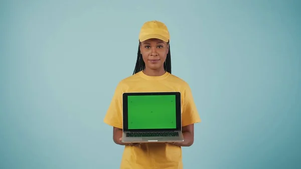 一个头戴黄帽 穿着T恤 手里拿着笔记本电脑 看着相机的送货妇女的画像 被蓝色背景隔离了广告区 工作空间模型 — 图库照片