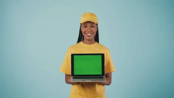 一个头戴黄帽 身穿T恤 手持笔记本电脑 对着相机微笑的送货妇女的画像 被蓝色背景隔离了广告区 工作空间模型 — 图库照片