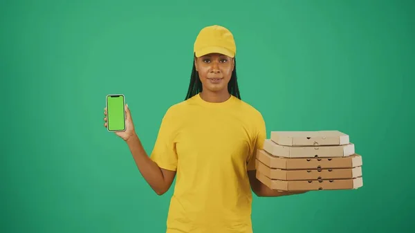 一个头戴黄帽 头戴T恤 拿着披萨盒和智能手机的送货妇女的画像 被绿色背景隔离 广告区 工作空间模型 — 图库照片