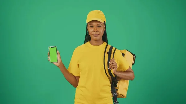 一个头戴黄色帽子 手持手提式背负式冰箱和智能手机的送货妇女的画像 被绿色背景隔离 广告区 工作空间模型 — 图库照片