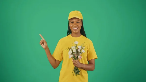 黄色い帽子とTシャツの配達女性の肖像画は 空の領域を指し 花束を保持しています 広告を挿入するスペース — ストック写真