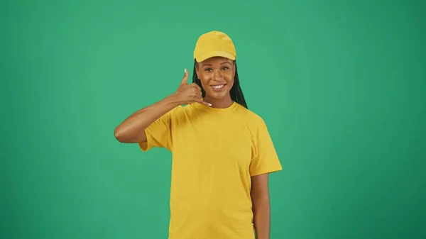 宅配サービスのコンセプト カメラで黄色い帽子とTシャツの配達女性の肖像画 呼び出しジェスチャーを示しています 広告を挿入するスペース — ストック写真