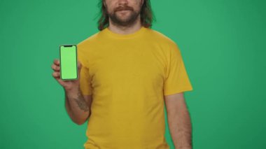 Yakın plan çekim. Elinde kahve tutacağı ve akıllı telefon tutan sarı şapkalı bir teslimatçının portresi. Paket servis ürünleri. Yeşil arka planda izole edilmiş. Reklam alanı, çalışma alanı modeli.
