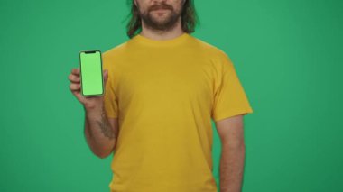 Yakın plan çekim. Sarı şapkalı bir teslimatçının portresi. Elinde banka kartı ve akıllı telefon var. Çevrimiçi ödeme. Yeşil arka planda izole edilmiş. Reklam alanı, çalışma alanı modeli.