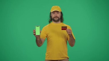 Kurye hizmeti konsepti. Sarı şapkalı bir teslimatçının portresi. Elinde banka kartı ve akıllı telefon var. Online ödemeler. Yeşil arka planda izole edilmiş. Reklam alanı, çalışma alanı modeli.