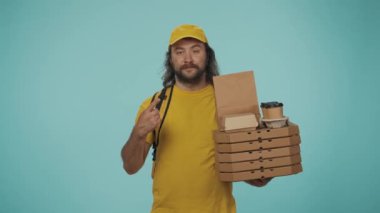 Kurye hizmeti konsepti. Elinde pizza kutuları, kahve ve boş bölgeyi gösteren sarı şapkalı bir teslimatçının portresi. Reklam için yer açın. Mavi arkaplanda izole.