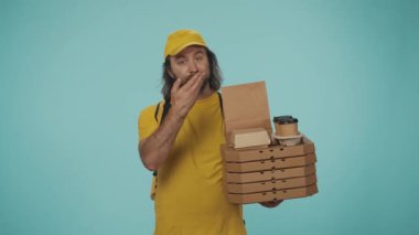 Kurye hizmeti konsepti. Sarı şapkalı bir teslimatçının portresi yemek siparişi veriyor ve boş alanı işaret ediyor. Reklam için yer açın. Mavi arkaplanda izole.