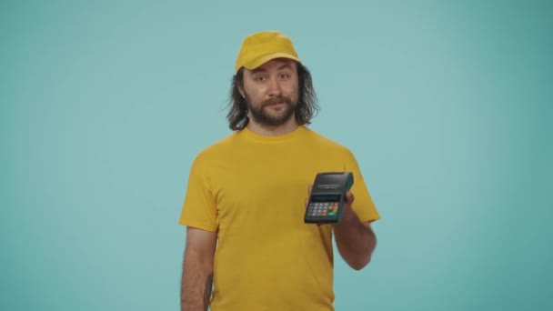 宅配サービスのコンセプト カメラを見ている携帯端末と銀行のクレジットカードを提供する黄色いキャップの配達男性の肖像画 オンライン決済 青い背景に孤立した — ストック動画