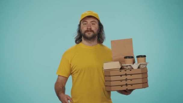 宅配サービスのコンセプト ピザ箱とコーヒーカップホルダーを保持している黄色いキャップの配達男性の肖像画は 呼び出しジェスチャーを示しています 食品を注文する 青い背景に孤立した — ストック動画