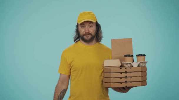 宅配サービスのコンセプト ポータブル決済端末を提供するピザ箱とコーヒーカップホルダーを保持している黄色いキャップの配達男性の肖像画 オンライン決済 青い背景に孤立した — ストック動画