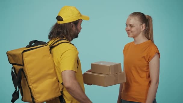 宅配サービスのコンセプト ポータブルバックパック付きの黄色い帽子の配達男性の肖像画は 女性の顧客パッケージを与え 少女はタブレットで注文に署名します 青い背景に孤立した — ストック動画