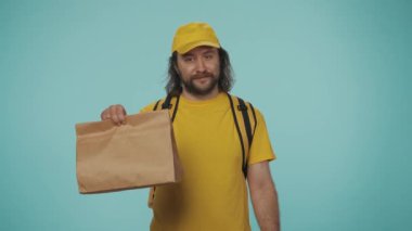 Kurye hizmeti konsepti. Sırt çantalı, çantalı, saati olan sarı şapkalı bir teslimatçının portresi. Mavi arkaplanda izole.