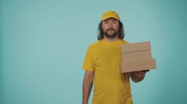 Kurye hizmeti konsepti. Sarı şapkalı bir teslimatçının portresi bir yığın posta kutusu tutuyor ve boş bölgeyi işaret ediyor. Reklam için yer var. Mavi arkaplanda izole.