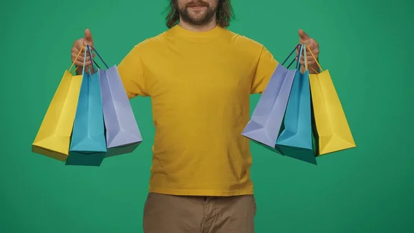 クローズアップショット カラフルな紙のギフトバッグを手に持っている黄色いシャツの配達男性の肖像画 緑色の背景に分離されています クーリエサービスコンセプト — ストック写真