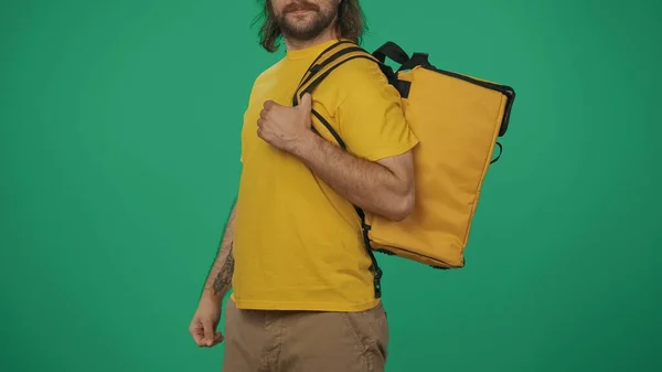クローズアップショット 食品用のポータブルバックパック冷蔵庫を持っている黄色いTシャツの配達男性の肖像画 緑の背景に孤立した — ストック写真