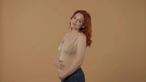 一个年轻的孕妇用手抱着她的大肚子的画像 在橙色背景下被隔离的孕妇的侧视图 母性和爱情的概念 — 图库照片