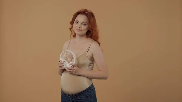 Una Mujer Embarazada Pelirroja Sosteniendo Auriculares Inalámbricos Blancos Una Mujer — Foto de Stock