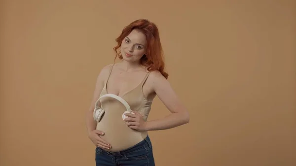 Una Mujer Embarazada Pelirroja Pone Auriculares Inalámbricos Blancos Vientre Una — Foto de Stock