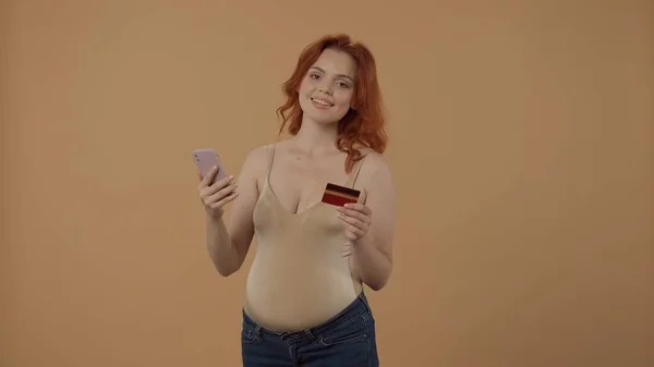 网上支付 一个孕妇在网上商店里用智能手机用信用卡购物 在一个橙色背景的工作室里怀孕的女人怀孕 母性概念 — 图库照片