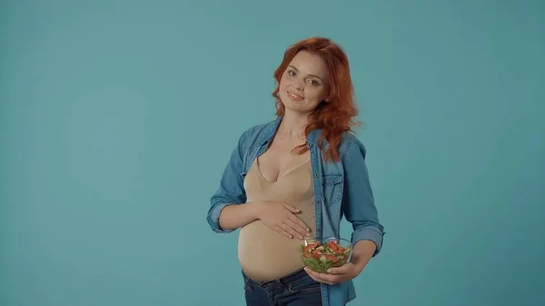 妊娠中の女性はサラダ付きの透明なガラスプレートを保持しています 青い背景のスタジオにいる女性 妊娠中の女性のための健康で適切な栄養 — ストック写真