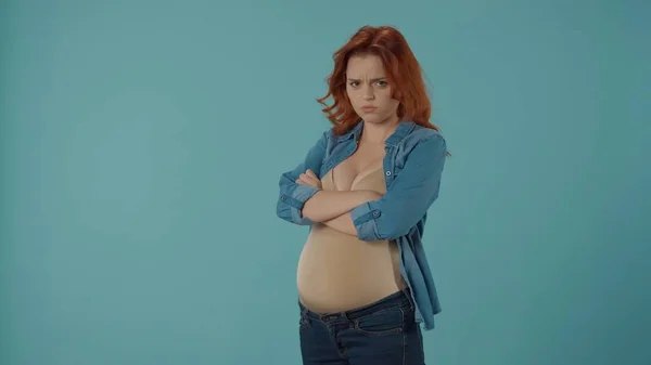 赤毛の妊婦が動揺し 怒っている 胸に腕を乗せた女性が青い背景のスタジオに立っている 妊娠と感情 変化する気分 ホルモン — ストック写真