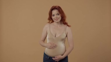 Kızıl saçlı hamile kadın göbeğini okşuyor ve turuncu arka planda meditasyon yapıyor. Kadın ellerini bir Mudra hareketiyle tuttu. Gözleri kapalı ve derin bir nefes aldı.