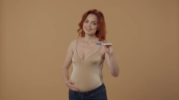 妊娠中の女性は 肯定的な結果で妊娠検査を受ける 女性が胃をストロークし オレンジ色の背景にあるスタジオで親指を示します — ストック動画