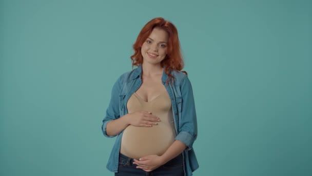 妊娠中の女性は サラダやケーキの皿を提供しています 女性は甘いデザートを選ぶ 青い背景のスタジオにいる女性 妊娠の渇望について — ストック動画