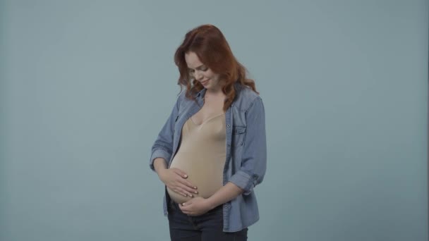 一个年轻的孕妇用爱心和柔情抚摸着她那肿胀的肚子 一个身披蓝色背景的孕妇在工作室的画像 母性和爱情的概念 — 图库视频影像