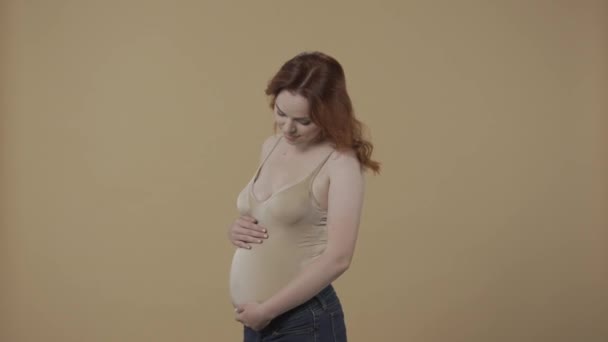 若い妊娠中の女性は 愛と優しさで彼女の膨大な胃を打っています オレンジ色の背景にあるスタジオの妊婦のプロフィール肖像画 そして — ストック動画