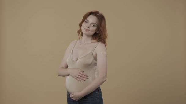 一名孕妇在注射疫苗后用补丁指向她的手 然后竖起大拇指 一个女人在一个橙色的背景下紧紧地抱着她那肿胀的肚子 — 图库视频影像
