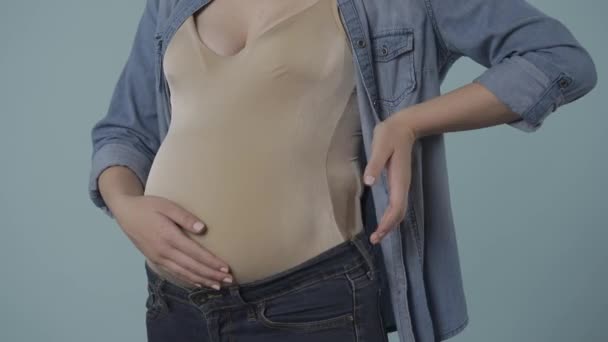 一个怀孕的女人用爱心和柔情抚摸着她肿胀的肚子 表现出心脏的迹象 双手放在肚子上 美女一个怀孕的女人在工作室里的蓝色背景特写 — 图库视频影像