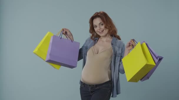 カラフルなショッピングバッグを閉じた幸せな妊婦の肖像画 妊娠中の女性はブルーで孤立しました 母性と妊娠の概念 — ストック動画