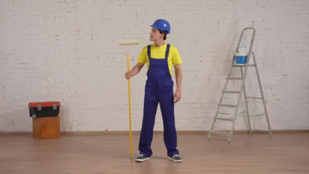 ローラーで部屋に立っている笑顔の若い労働者の完全な長さのビデオ 新鮮に塗られた壁を見て 親指を上げます メーカー 会社広告 — ストック動画